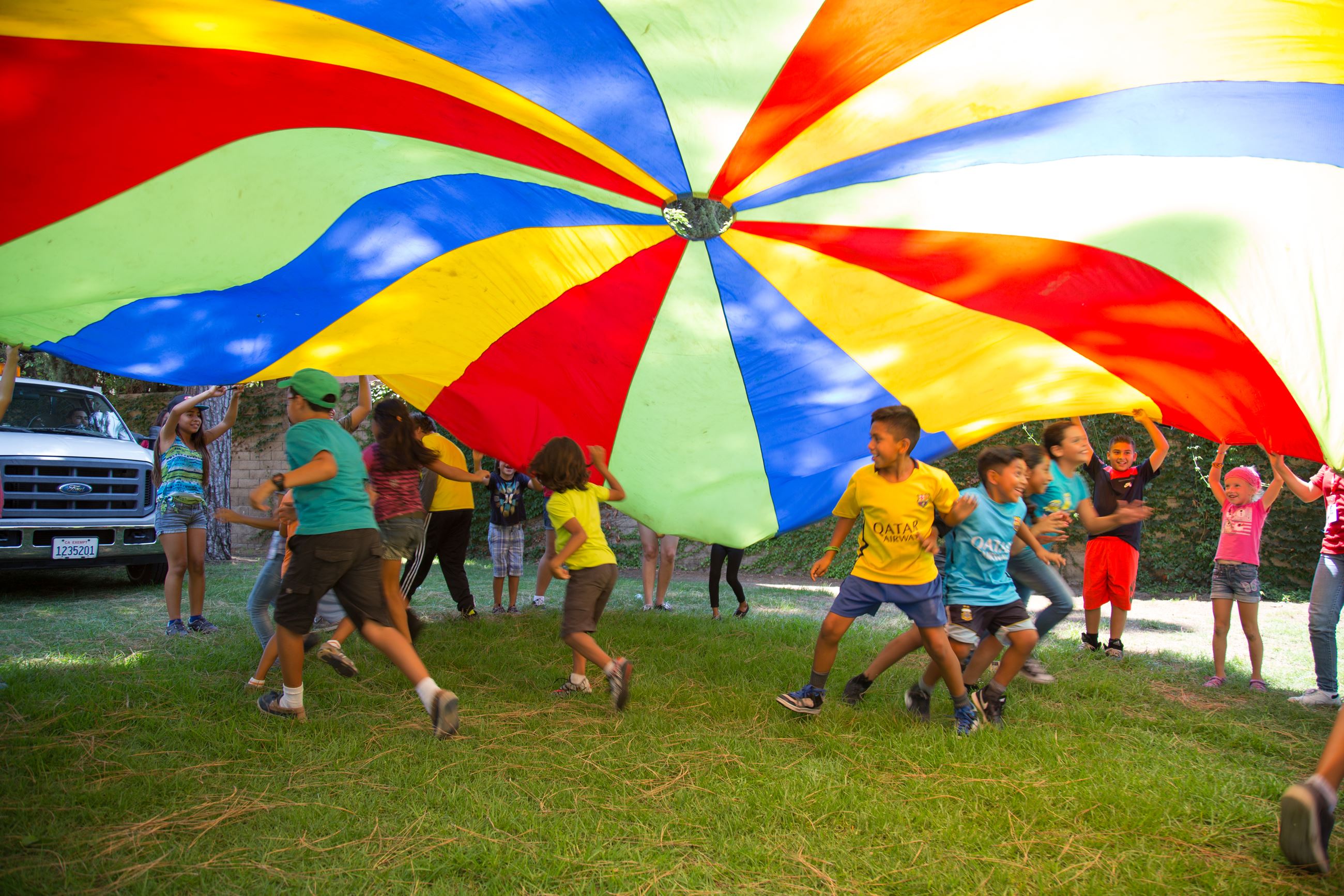 Children running under a rainbow colored parachute.