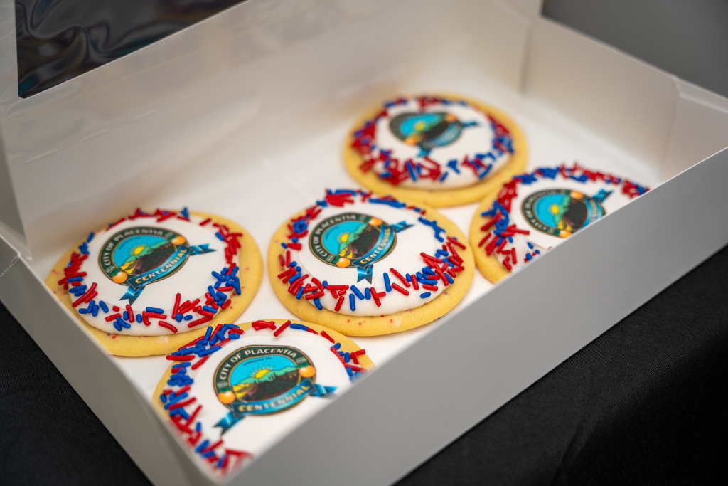 Five decorated sugar cookies with a printed City of Placentia Centennial logo and red and blue sprin…